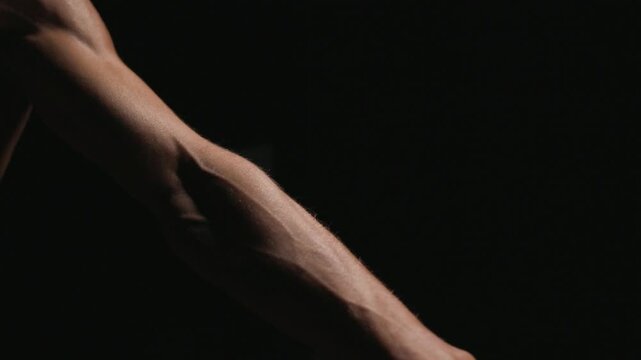 Close-up toned female torso during spray tanning session with gloved hand and spray gun under dramatic lighting from left side revealing sculpted abdominal muscles