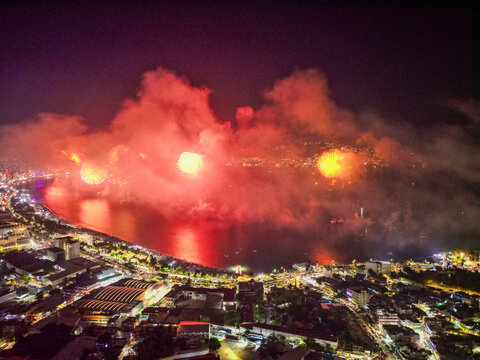 Spectacular drone view of New Year fireworks exploding over Acapulco Bay at night, illuminating the vibrant city skyline and reflecting on the water, a festive celebration.