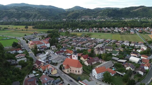 Static aerial drone footage of Limbus Parish Church with its red tiled roof and bell tower, surrounded by residential houses and woodland in Limbus, Slovenia.