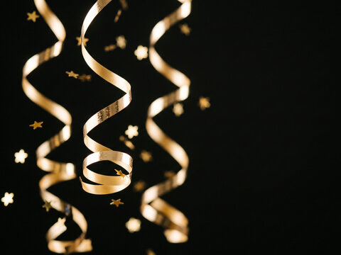 Champagne gold metallic streamers and star confetti frozen in motion on black, New Year party background