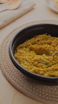 Freshly Cooked Yellow Moong Dal Khichdi with Turmeric Served Hot in a Black Bowl, Close-Up Food Shot of being picked with a spoon.