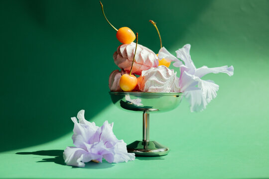 Dessert with meringue, cherries, and flowers on a green background