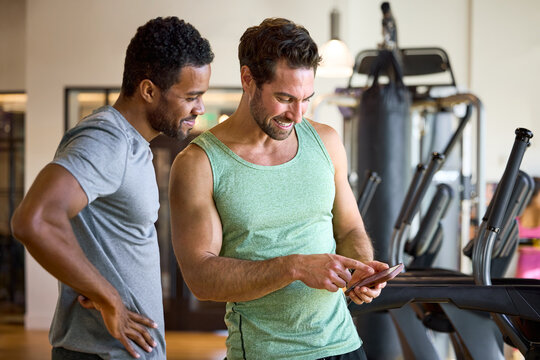 Two men checking treadmill stats at gym workout tracker & planner app