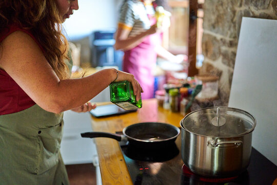 Woman pouring oil into frying pan on stove