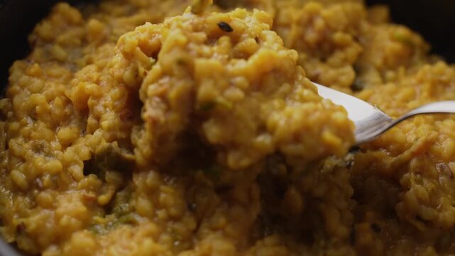 Freshly Cooked Yellow Moong Dal Khichdi with Turmeric Served Hot in a Black Bowl, Close-Up Food Shot of being picked with a spoon.