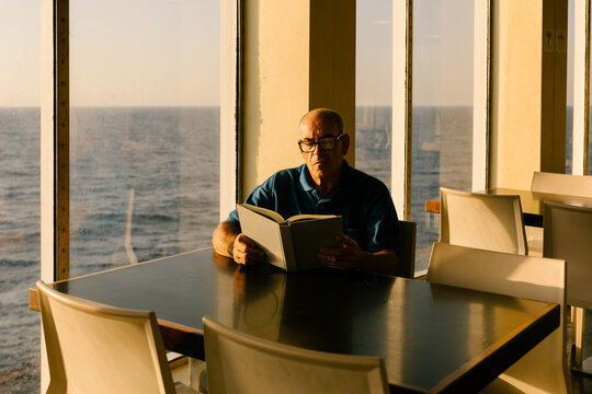 Man engrossed in reading a book, sitting right next to a window