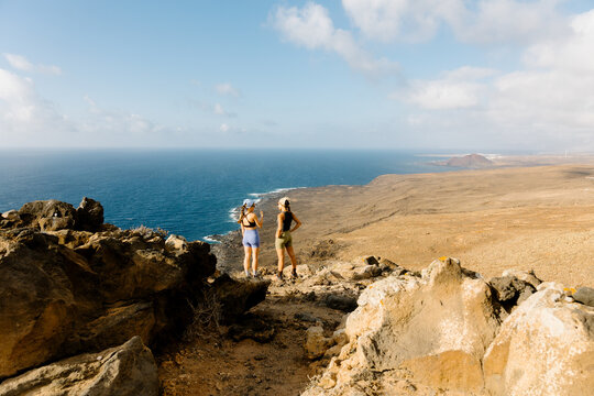 A wide shot of two fit women in athletic wear standing high on a cliff