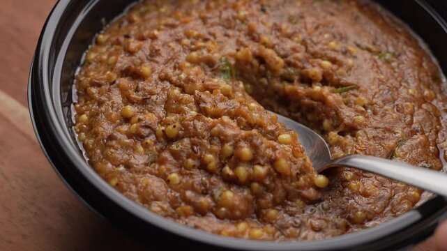 Freshly Cooked Healthy Millet Khichdi Served Hot in a Black Bowl, Close-Up Food Shot of being picked with a spoon.