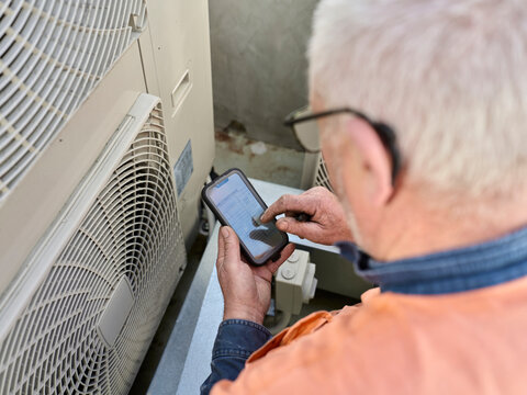 Worker Uses Smartphone Near Air Conditioning Unit