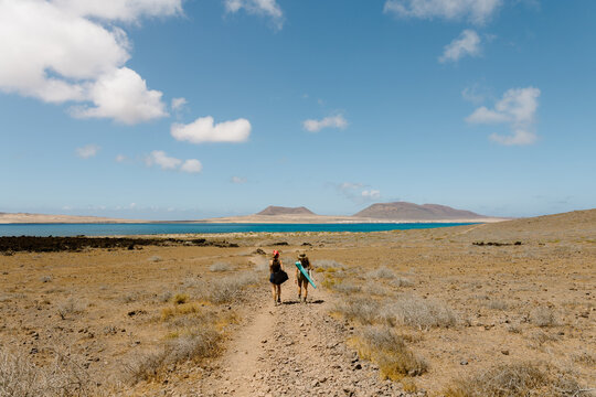Two female friends walking toward the sea on a sunny Lanzarote coast.