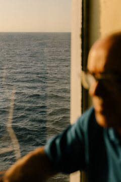 Blurred figure relaxing by a ship porthole during an ocean sunset.