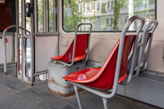 Old red passenger seats inside vintage tram with worn metal frames and empty interior, close up