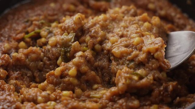 Freshly Cooked Healthy Millet Khichdi Served Hot in a Black Bowl, Close-Up Food Shot of being picked with a spoon.
