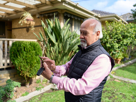 Elderly Man Uses Phone While Standing in Front of House