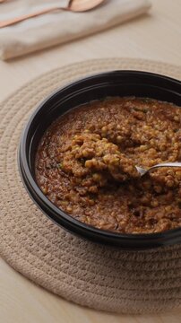 Freshly Cooked Healthy Millet Khichdi Served Hot in a Black Bowl, Close-Up Food Shot of being picked with a spoon.
