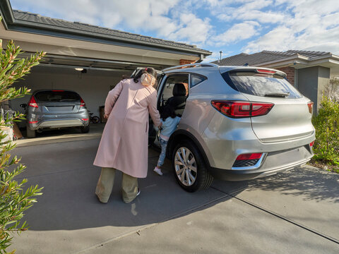 Mother Helps Child into Car on Driveway