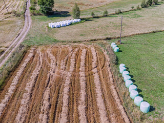 Naklejka premium Wrapped silage bales lined along harvested hay field edge, aerial drone view. Farming concept.