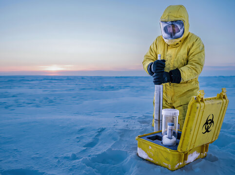 Researcher in a yellow protective suit holds a sampler beside a biohazard case and a sealed specimen container on a snowy polar plain. Concept of permafrost research and biological sample containment.