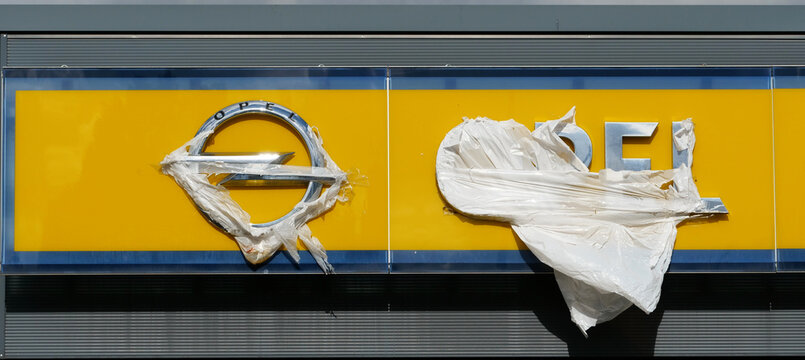 Germany, Salzkotten, October 10. 2026, official yellow company sign from an Opel dealership, on which the brand logo (the Opel lightning bolt) and the lettering are partially covered with shredded 