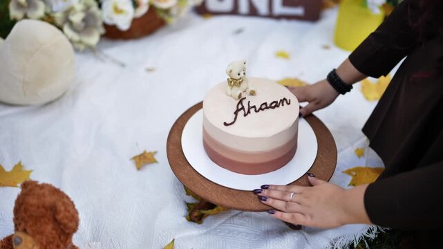 Woman's hands placing Ahaan's first birthday cake with a teddy bear topper on a wooden stand