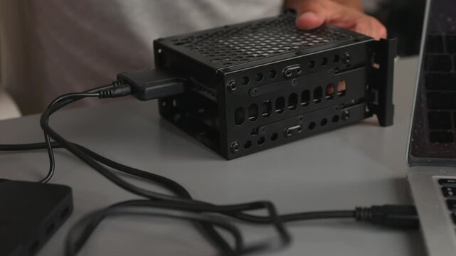 Hands connecting external hard drive enclosure to laptop with USB cable on tabletop, closeup of portable storage setup and hardware connection view from slight overhead angle, neutral soft lighting, t