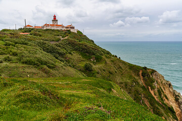 Fototapeta premium Cabo da Roca dramatic coastal cliff overlooking Atlantic Ocean in Portugal. Scenic westernmost point of Europe with rugged landscape, ocean waves and natural coastline.