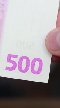 Vertical video close up. Fingers holding edge of 500 euro bill paper banknote with pink magenta foil security symbol. Five hundred. Pay tax, credit, debt, loan. Cash money of EU or European Union bank