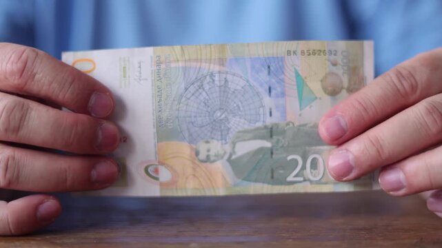 4K video close up. Front view. Male hand holds Serbian paper banknote 2000 dinar bill with portrait of climatologist Milutin Milankovitch and illustration from one of his works. Cash money, bank note