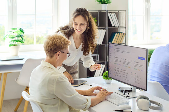 Adults students teacher instructor computer learning training. Friendly instructor guides a senior at a desktop in a bright classroom course for seniors. Lifelong learning and digital upskilling.
