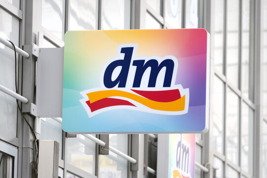 Berlin, Germany - 16 August 2026. A colorful dm (drogerie markt) drugstore sign closeup with its distinctive logo against a backdrop of a gray building. Retail, shopping, storefront signage.
