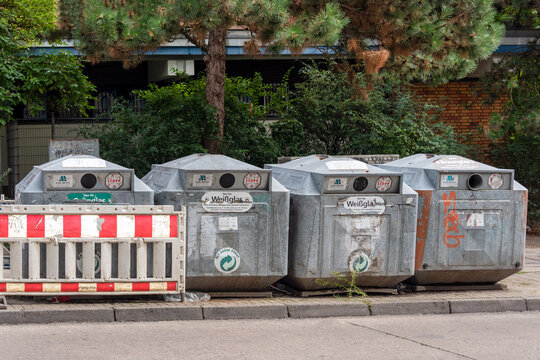 Berlin, Germany - 16 August 2026. Metal recycling containers stand on a city sidewalk behind a red-and-white barrier. Urban recycling, waste management, pollution, environment