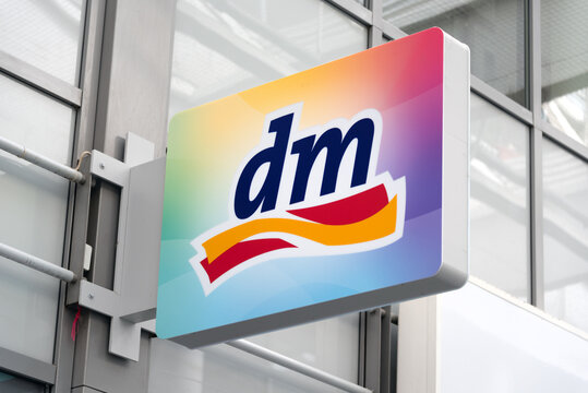 Berlin, Germany - 16 August 2026. A colorful dm (drogerie markt) drugstore sign closeup with its distinctive logo against a backdrop of a gray building. Retail, shopping, storefront signage.