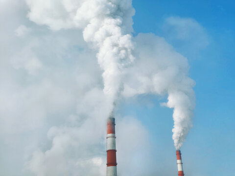 White smoke rising from industrial chimneys against blue sky