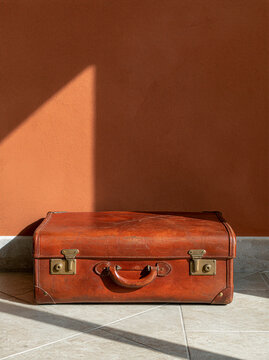 Vintage leather suitcase with worn brass hardware resting on tiled floor