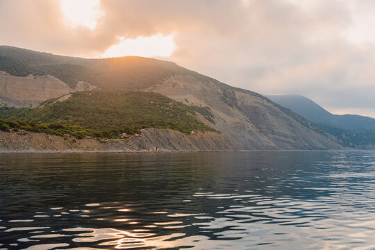 Sunset reflects across a calm sea surrounded by rugged hills, creating a peaceful travel landscape.