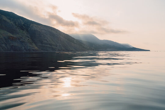 Warm sunset light reflects on sea creating a serene landscape with dramatic hills and open water.