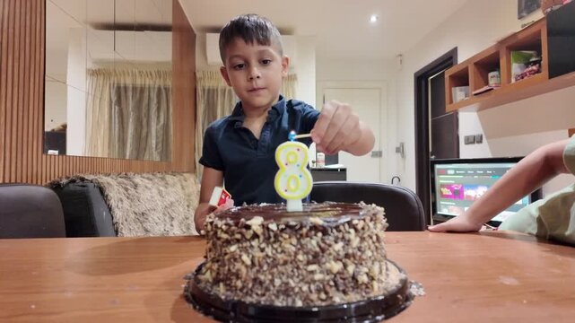 Young boy lights birthday candle on chocolate cake. Second boy smiles beside him. Warm indoor lighting highlights joyful moment. Perfect for birthday, family, or celebration themes