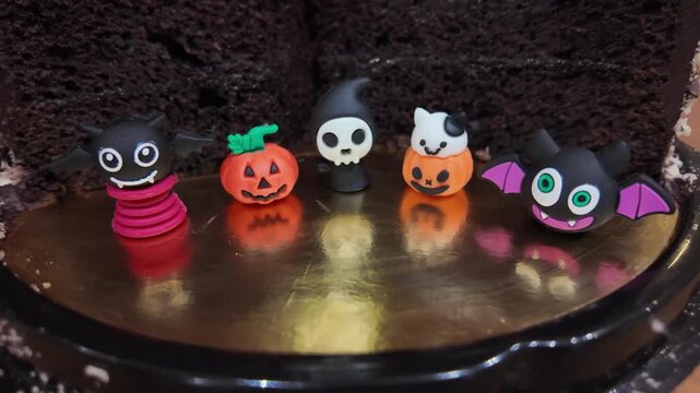 Dark chocolate cake slices shown. Mini figures decorate the cake. Small pumpkins, ghosts, and bats adorn the cake. Child watches from background. Halloween celebration scene