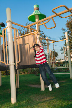 Happy child playing on monkey bar holding with hands swinging at outdoor playground during sunny day
