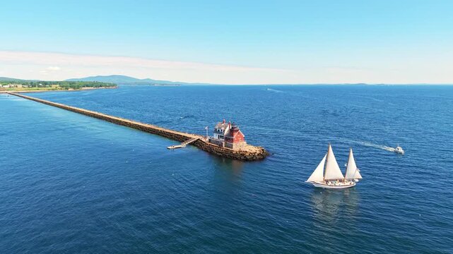 Aerial view of a two-masted schooner sailing past Rockland Breakwater Light and the long granite breakwater in Penobscot Bay near Rockland, Maine.