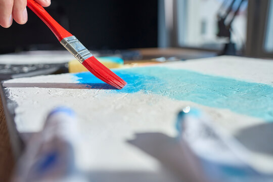 Close up of brush spreading blue paint across textured canvas. Creative hobby and painting process