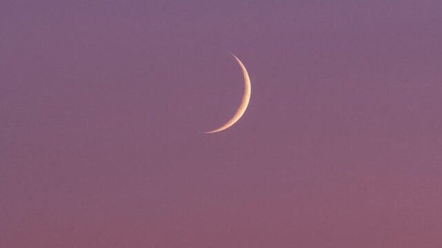 Time lapse of crescent moon rising against cloudless night sky above horizon.
