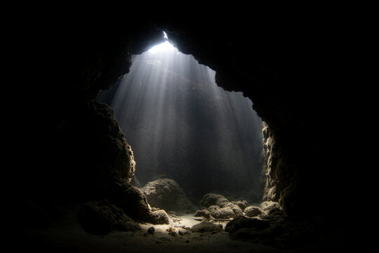 Sunlight enters a dark, underwater cavern on a coral reef growing around a remote, tropical island in Indonesia. Coral reefs are riddled with cracks, fissures, tunnels, and caves.
