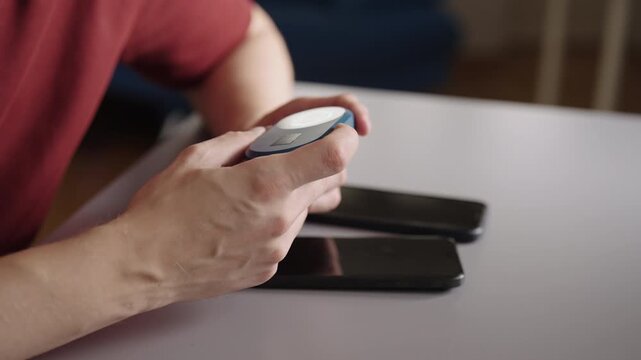 Male hands holding pocket sized wi fi router, sharing mobile data connection with two smartphones resting on table, concept of portable internet access, close-up, slow motion.