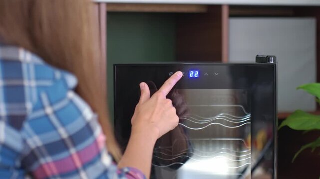 Woman adjusting temperature on wine cooler after unpacking it. Setting up new home appliance
