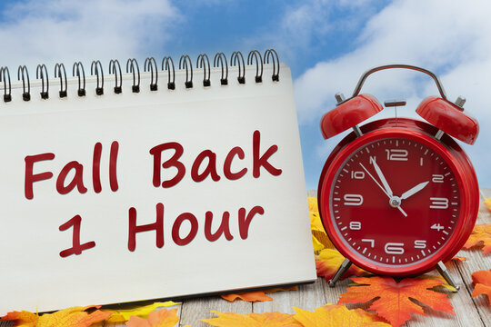 DST daylight saving time with Fall Back 1 Hour with fall leaves and alarm clock on wood