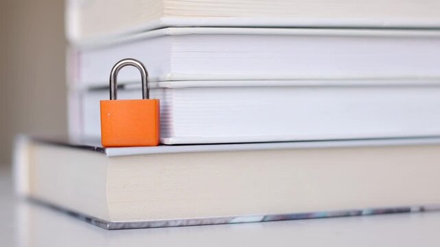 Orange padlock securing a stack of books, symbolizing censorship, restricted information, freedom of speech, and limitations on access to knowledge.