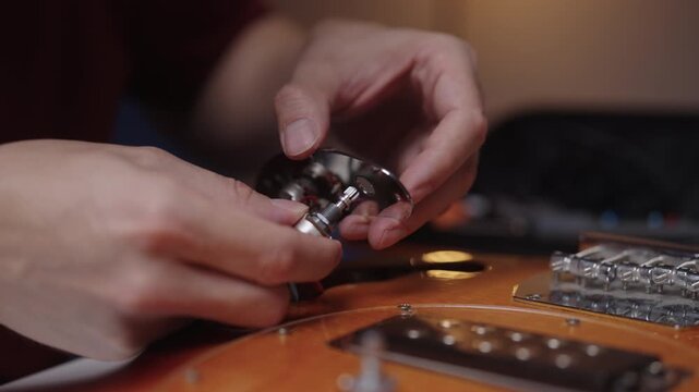 Professional musical instrument maker assembling potentiometers and switch onto metal control plate of new electric guitar, showing precision craftsmanship, close-up, cropped shot, slow motion.