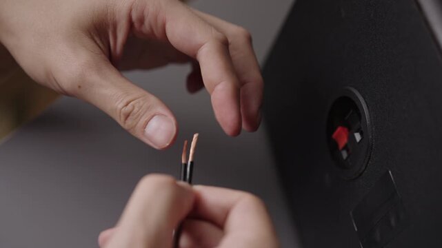 Close-up of hands preparing speaker cable. Person twists bare copper strands of audio wire before connecting to sound system. DIY home entertainment setup and hi fi installation concept, slow motion.
