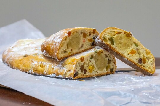 Christstollen, traditional German Christmas fruit bread dusted with powdered sugar and cut into slices, showing the dense crumb studded with candied cherries, candied fruit, raisins and nuts, on a rus
